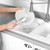 Washing up brush cleaning a white plate in kitchen sink with running tap