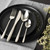 Four-piece silver cutlery set with patterned handles on black plate, styled with flowers