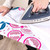 Person ironing white fabric on ironing board with pink and blue pomegranate print cover