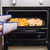 Oven tray with potato wedges and onion rings being placed in oven with oven gloves