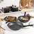 Set of black and white non-stick pans and pots with food on a kitchen worktop