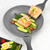 Grey frying pan with grilled salmon fillets, asparagus, cucumber and tomato, top-down view