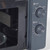 Close-up of black microwave oven with open door, showing control dials and glass turntable.