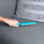 Hand using turquoise pet hair remover brush on grey sofa cushion