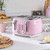 Pink 4-slice toaster with controls, two seeded bread slices toasting, hand pressing lever