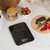 Black digital kitchen scale weighing chocolate pieces on worktop with granola and strawberries