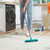 Teal rubber broom head being rinsed under a kitchen tap in a white sink.