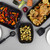 Set of three black roaster trays with chicken and vegetables on a kitchen worktop