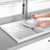 Stainless steel sink grid being cleaned with a dish brush in a white kitchen sink