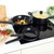 Set of three non-stick black pans on electric hob, one with glass lid and cooked pasta
