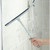 Hand using blue shower squeegee on glass for cleaning, shown in tiled bathroom.
