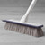Blue and white floor brush with long handle leaning against wall on laminate flooring