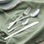 Set of silver cutlery including knife, fork, and two spoons on green textured cloth