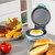 Mini blue electric grill with fried egg cooking, burger and breakfast food beside