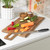 Wood chopping board with knife, carrot, courgette and chillies on white kitchen worktop