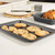 Non-stick grey baking tray with six chocolate chip cookies on kitchen worktop