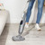 Steam mop cleaning light wood floor in living room, person shown from waist down