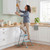 Woman using folding step ladder in modern kitchen to reach high cupboard