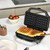 Black waffle maker with two golden waffles on kitchen worktop, hand lifting one waffle.