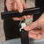 Close-up of hands attaching a black luggage strap to a suitcase using a metal clip