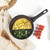 Set of three black non-stick frying pans, one with salmon and asparagus, one with omelette and greens, on kitchen worktop.