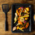 Roasting tray with assorted cooked vegetables beside black handled spatula on wooden surface