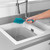 Blue silicone washing up brush being rinsed under tap in a kitchen sink