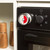 Mechanical kitchen timer attached to oven, red and silver, with wooden grinders nearby