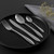 Four-piece silver cutlery set on black plate, knife, fork, spoon and teaspoon.