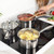 Set of three stainless steel saucepans with glass lids on an induction hob, in use.