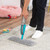 Spray mop with blue handle cleaning light rug, shown in use on wooden floor