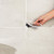 Hand using cleaning brush on light grey tile grout