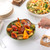 Serving bowl of roasted mixed vegetables with hand holding spoon, next to pasta salad