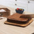 Square chocolate cake being sliced on a wooden board in a kitchen, with baking tin nearby