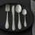 Four-piece silver cutlery set on black plate, including fork, knife, spoon and teaspoon