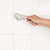 Hand cleaning white tiled grout with angled cleaning brush