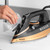 Copper and black steam iron being filled with water at a kitchen sink