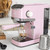 Pink espresso coffee machine in kitchen making coffee, shown with milk jug and scoop.