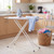 Ironing board with iron and blue shirt in laundry room, basket of clothes nearby