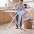 Person ironing a blue shirt on patterned ironing board in a kitchen, laundry basket nearby