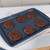Six chocolate cookies on a baking tray, shown fresh from the oven.