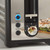 Black and silver toaster with illuminated reheat and defrost buttons, close-up