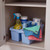 Cleaning kit with spray, wipes, gloves and cloths in blue caddy under a cupboard