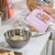 Hand holding pink electric hand mixer blending dough in metal bowl on kitchen counter