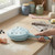 Blue electric pancake maker on kitchen counter, flour and eggs beside, hand holding handle
