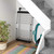 Folding metal pet gate stored under stairs, next to cleaning tools and plant