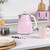 Pink electric kettle with handle on kitchen counter, cup and coffee jar nearby