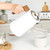 White electric kettle with wood handle pouring hot water into mug, kitchen setting.