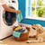 Person loading washing machine with basket of colourful clothes and dog in foreground