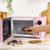 Hand placing bowl of chocolate pieces into pink microwave on kitchen counter